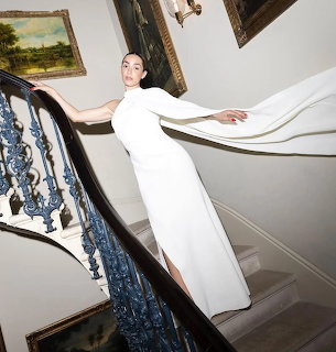 Woman in white floor-length gown standing on decorative staircase with blue patterned carpet