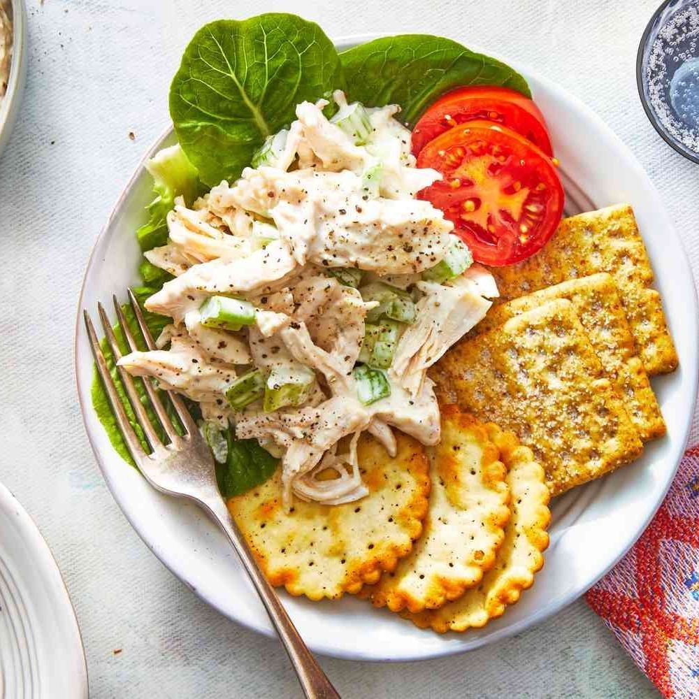 Overhead view of chicken salad plate with tomatoes, crackers, and greens on white plate
