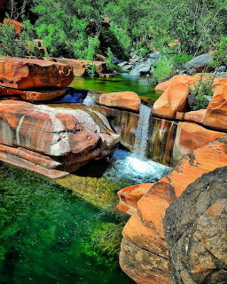 Emerald green pool surrounded by red sandstone rocks with small waterfall and green vegetation