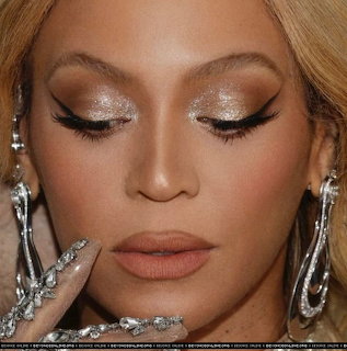 Close-up of woman with gold eyeshadow, winged eyeliner, nude lips, and silver jewelry