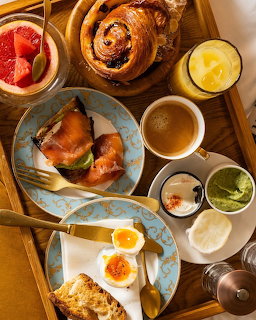Overhead breakfast spread with pastries, eggs, salmon, coffee and juice on wooden table
