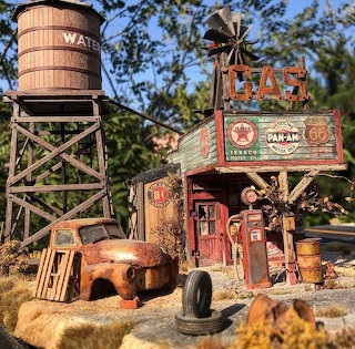 Miniature vintage gas station with old truck, gas pumps, and a water tower outdoors