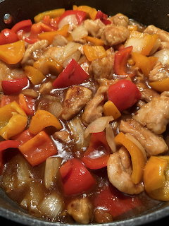 Close-up of orange chicken stir-fry with peppers and pineapple in a dark pan