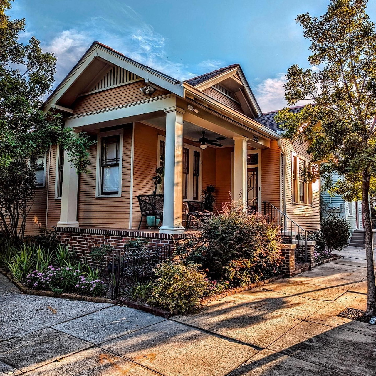 Craftsman-style house with covered porch, white columns, and landscaped front yard at golden hour