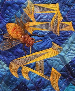 Detailed quilt section with golden embroidered bees on blue quilted fabric