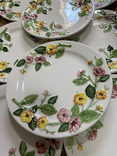 White ceramic plates decorated with hand-painted pink, yellow, and purple flowers on floral tablecloth