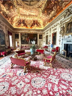 Lavish historic room with painted ceiling, gilded walls, red upholstered furniture, and ornate patterned carpet