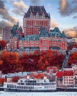 Château Frontenac castle hotel in Quebec City surrounded by red autumn trees with a riverboat below