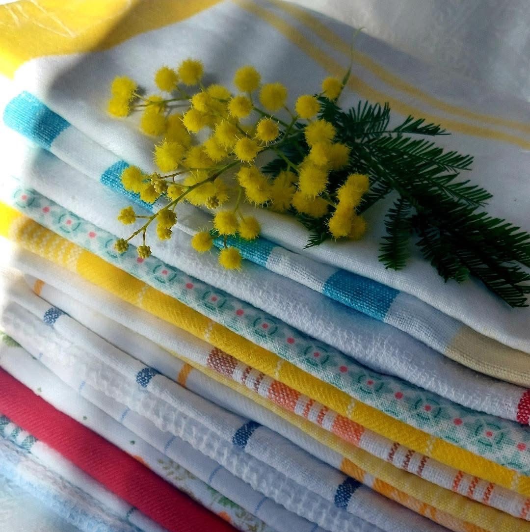 Stack of patterned kitchen towels with yellow mimosa flowers and fern on top