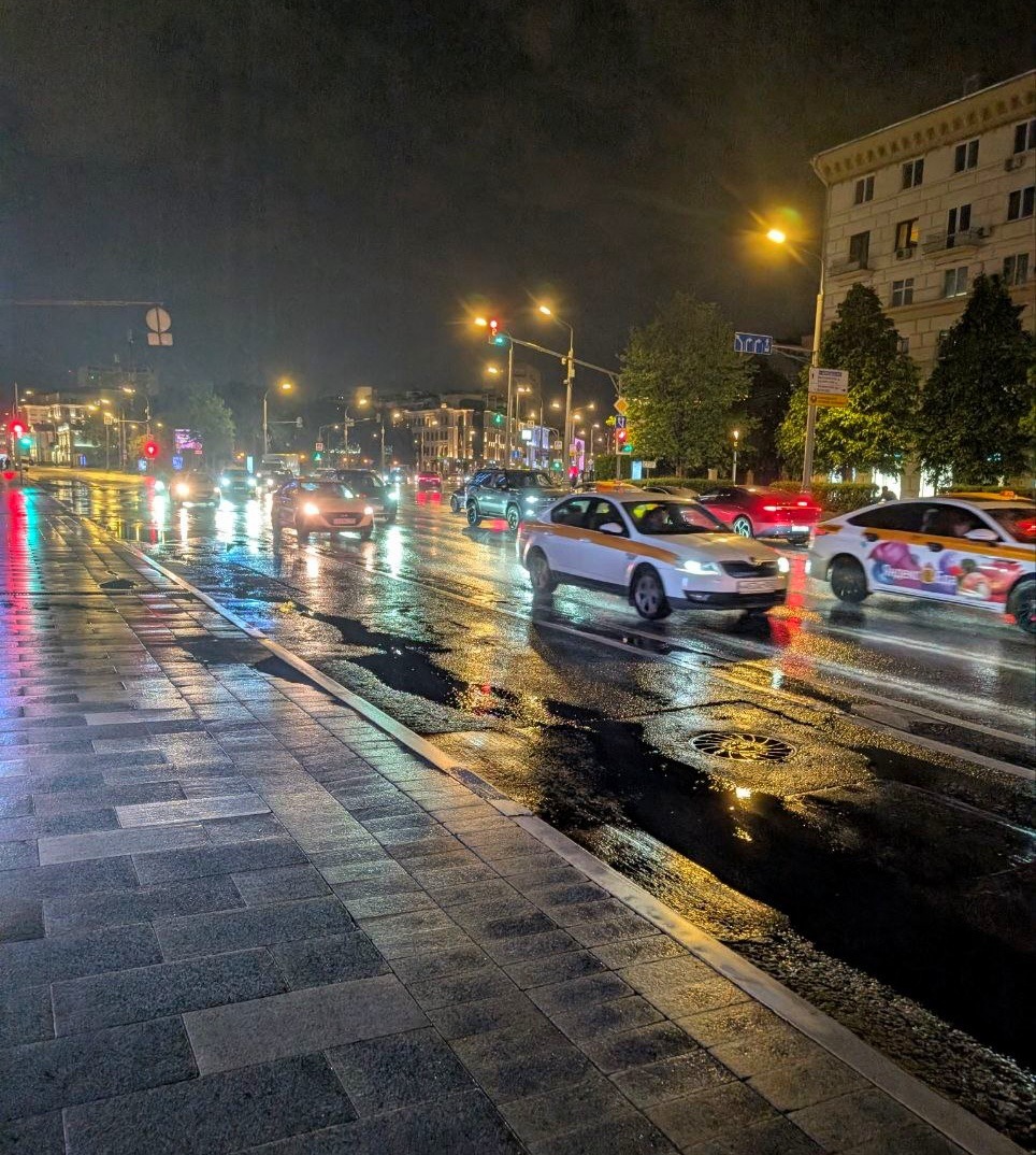 Rainy city street at night with cars and bright reflections on wet pavement