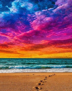 Sandy beach with footprints leading to ocean under a colorful rainbow sky with dramatic clouds