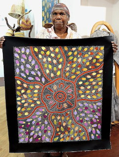 Indigenous Australian woman displaying a colorful Aboriginal dot painting with circular patterns on black fabric