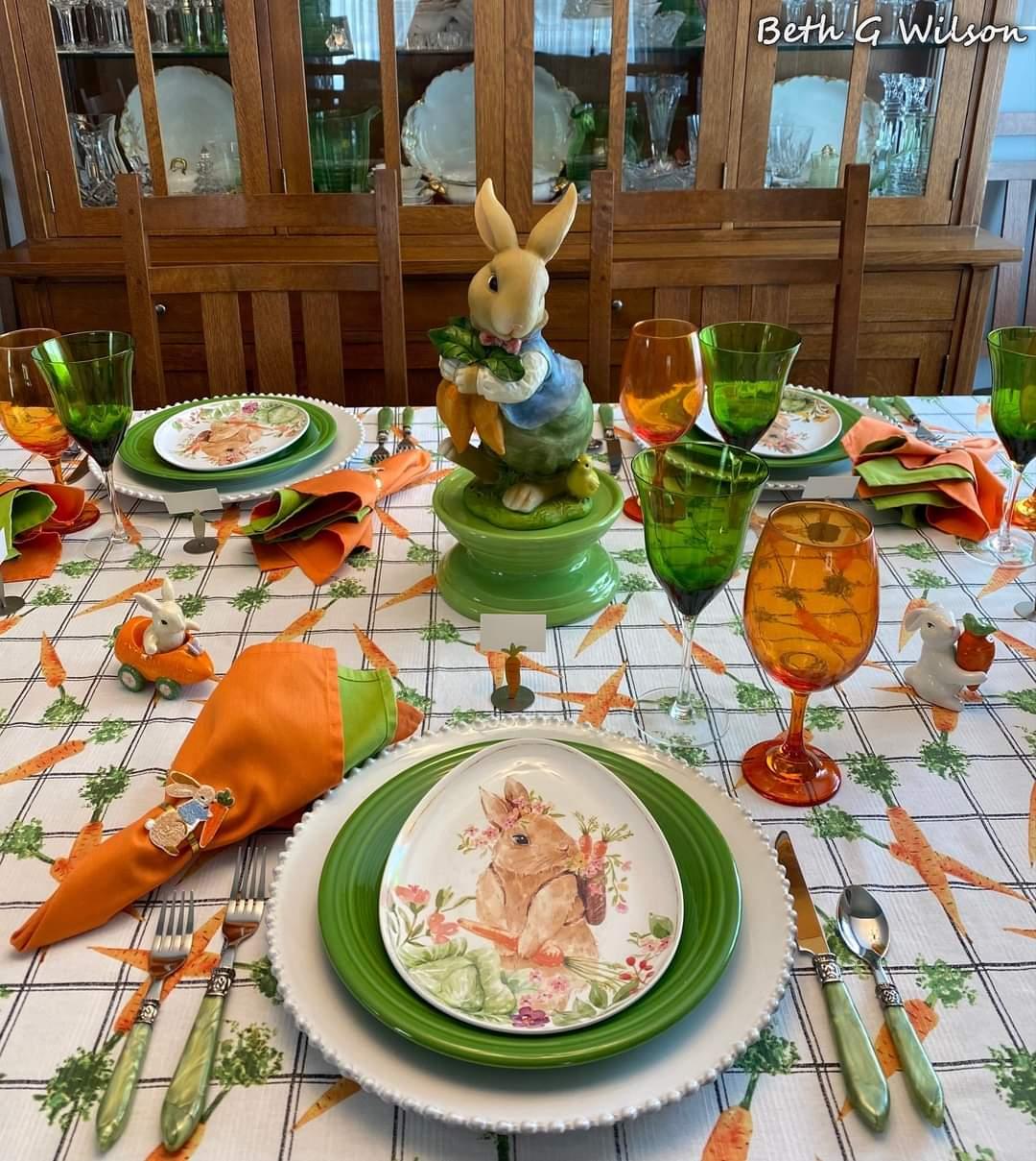 Easter table setting with bunny centerpiece, green plates, orange napkins, and carrot decorations