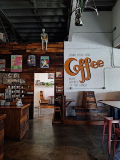 Rustic coffee shop interior with wooden walls, booths, skeleton decor, and a large Coffee sign on white wall