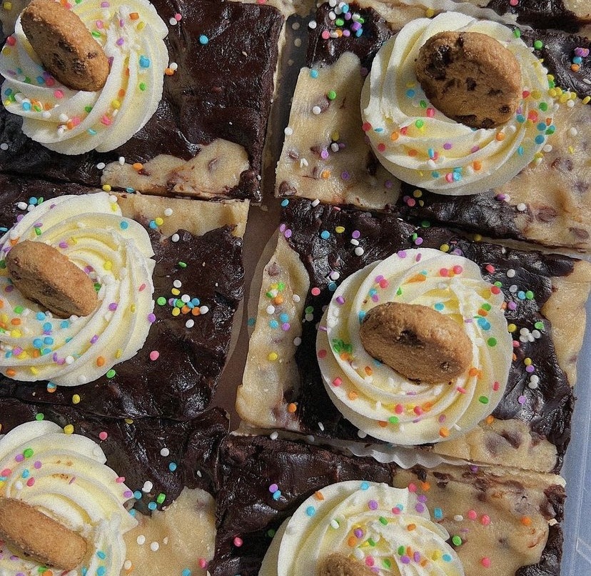 Brownie squares topped with whipped cream, cookie pieces, and colorful sprinkles