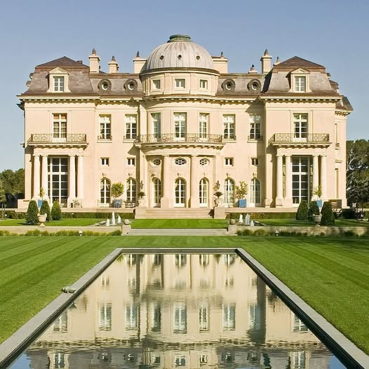 Symmetrical cream stone mansion with ornate architecture reflected in formal rectangular pool