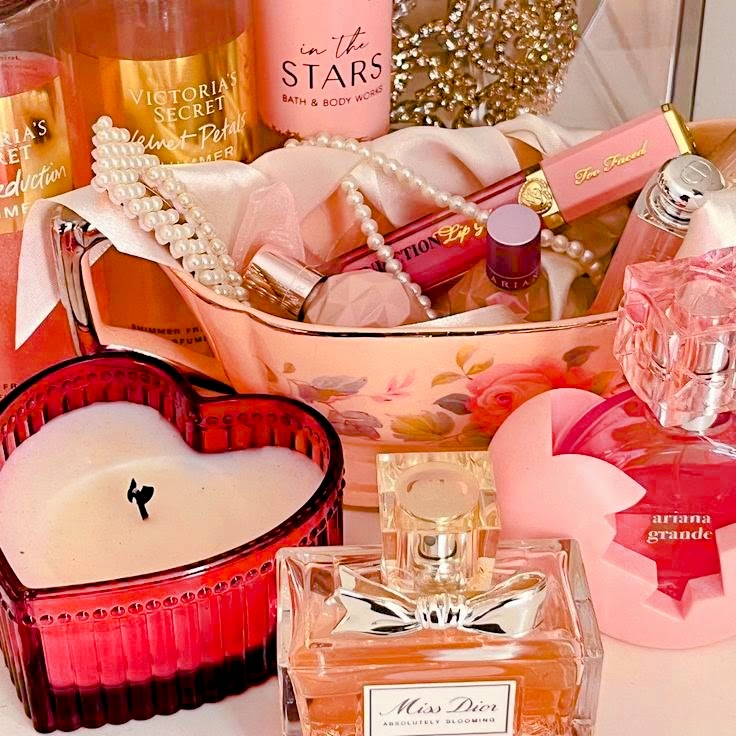 Pink vanity arrangement with perfume bottles, lipstick, a heart-shaped candle, and decorative accessories