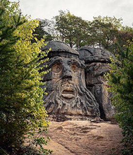 Carved stone face in a sandstone cliff surrounded by green trees
