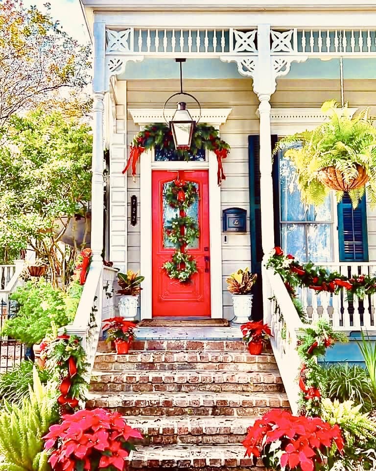 White cottage porch with classic red door, brick steps decorated with red poinsettias and holiday wreath