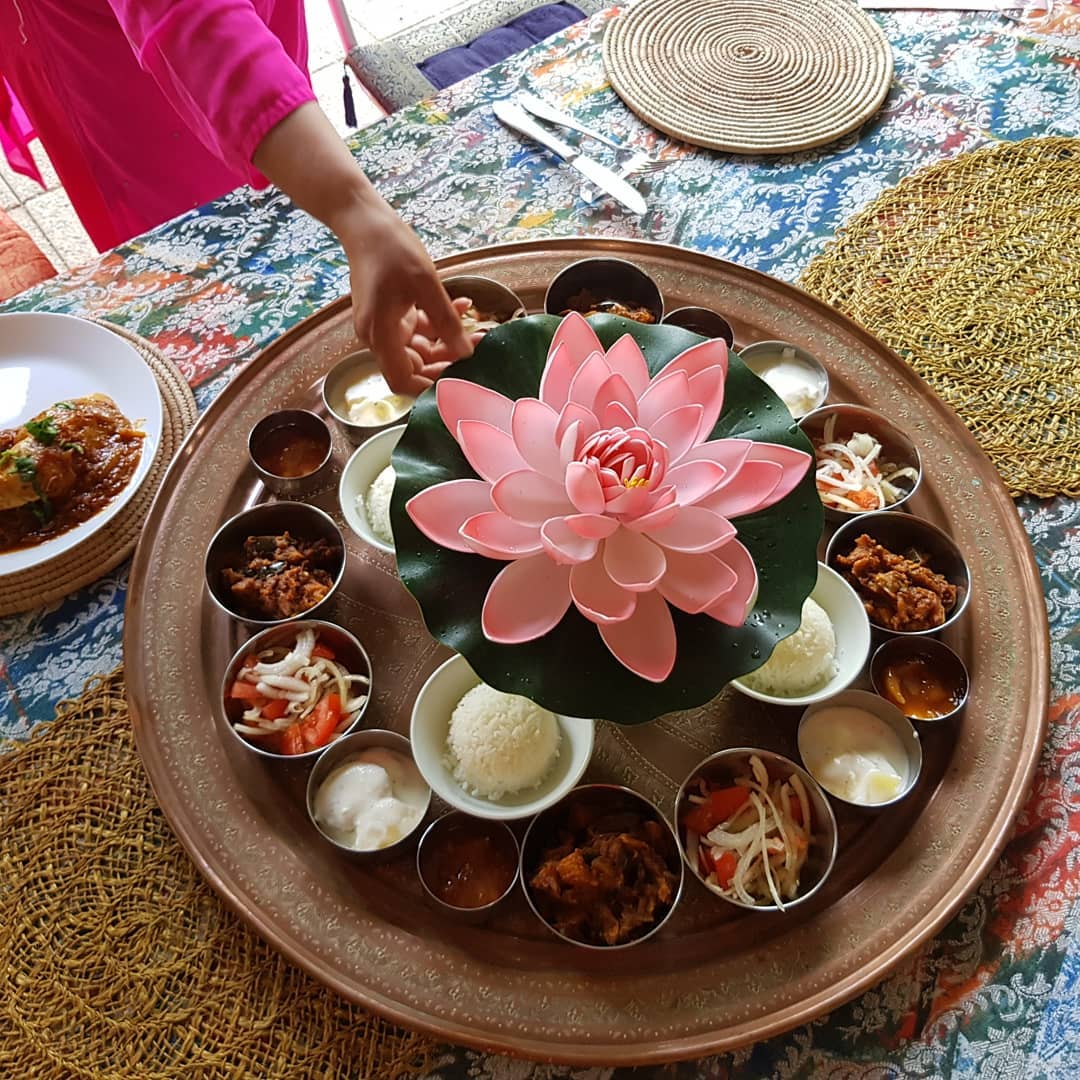 Indian thali platter with lotus centerpiece and small bowls of food arranged in circle