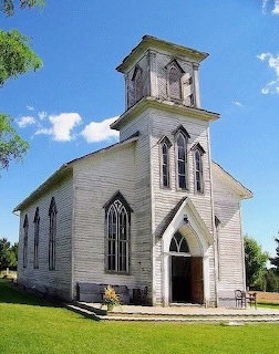 Old white wooden church with bell tower and gothic arched windows on a green lawn