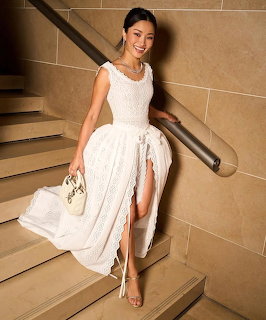 Woman in white dress sitting on staircase holding flowers