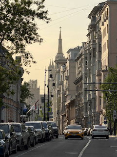 Urban street with parked cars, tall buildings, and a spired tower in the distance