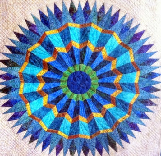 Circular quilt with blue, turquoise, and orange radial pattern