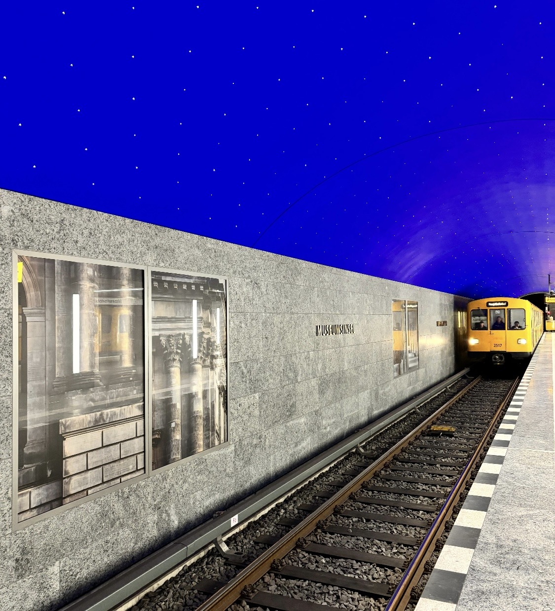 Metro train at illuminated underground platform with blue starry ceiling