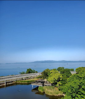 Curving bridge by a calm blue lake with green trees and distant hills under a clear sky