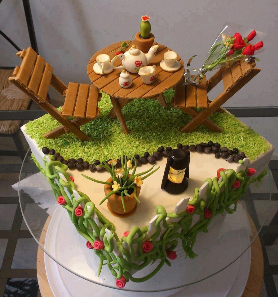 Decorated cake topped with a miniature table, chairs, cupcakes, flowers, and a lantern