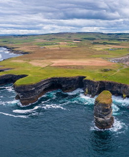 Aerial view of rugged Irish coastline with sea stack and green farmland