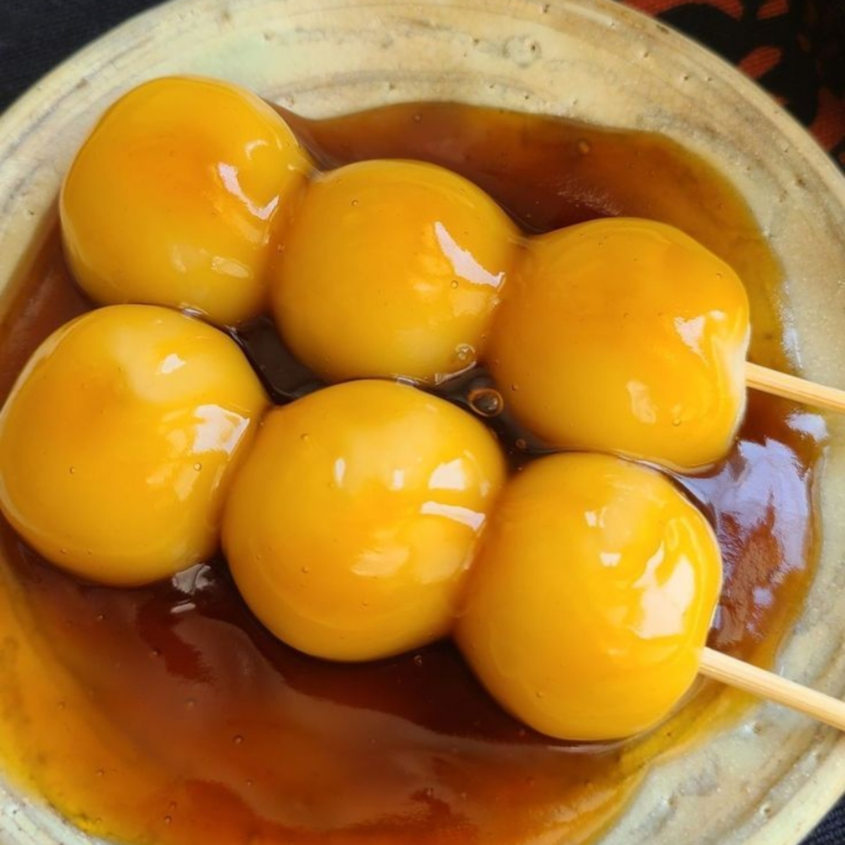 Three skewers of mitarashi dango with glossy brown sauce in a ceramic bowl