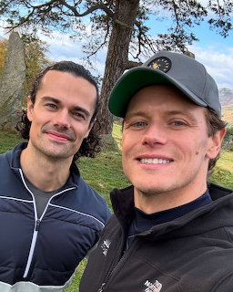 Two smiling men posing for an outdoor selfie near a tree.