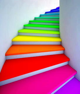 Colorful staircase with rainbow-painted steps ascending from red through orange, yellow, green to blue