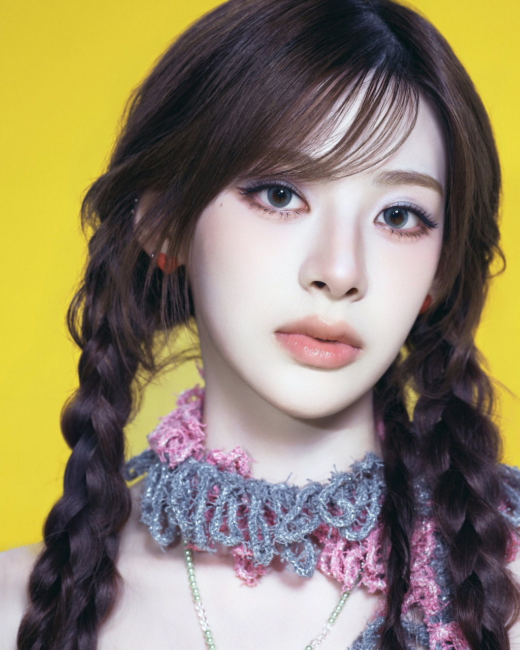 Young woman with braided pigtails and beaded necklace on yellow background