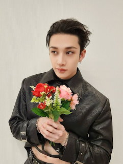 Young man in black leather jacket holding red and pink flower bouquet, portrait photo