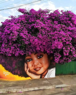 Street mural showing woman with purple flower afro against blue sky