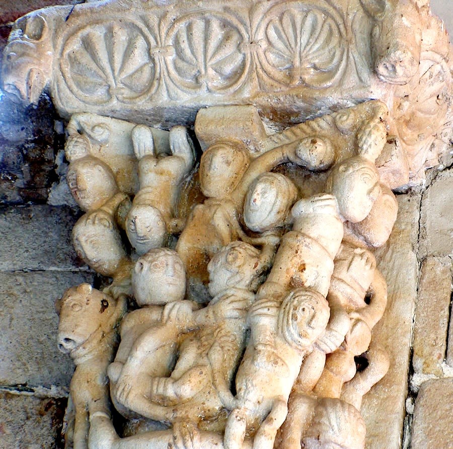 Close-up of an old stone capital with carved figures and shell motifs