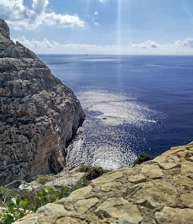 Rocky coastal cliff overlooking a calm blue sea with sunlight reflecting on the water