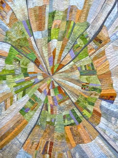 Colorful quilt with radiating strips forming a starburst pattern in orange, green, blue and yellow tones