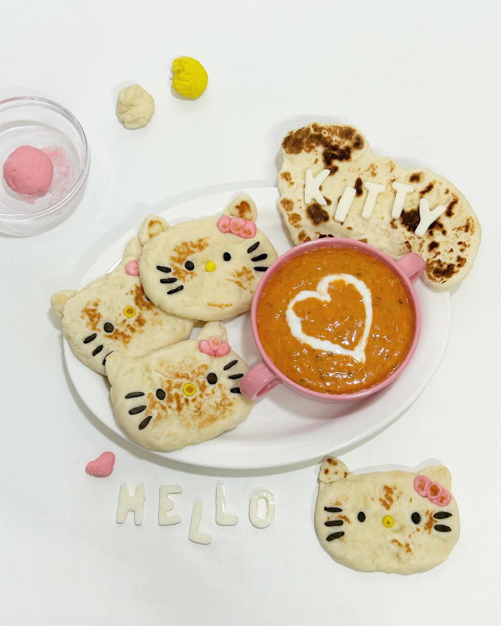 Hello Kitty shaped naan breads around a bowl of curry with heart design on a white plate