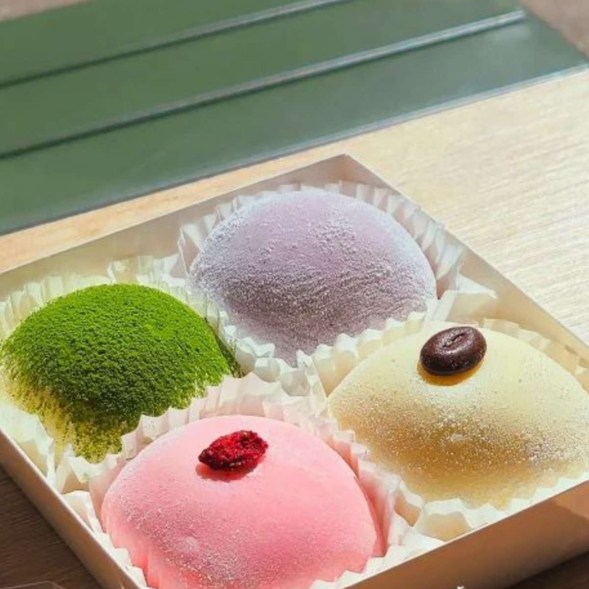 Four assorted mochi in a box with green, pink, purple, and white colors