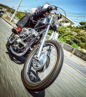 Custom chopper motorcycle with extended front fork riding on road, low-angle perspective