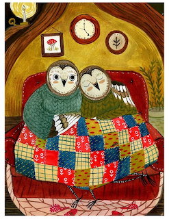 Two owls cuddled under a patchwork quilt on a red couch with framed pictures on the wall