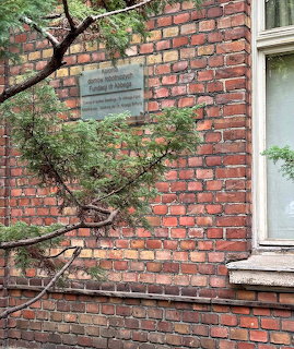 Red brick building wall with memorial plaque, pine tree branches, and a white window frame