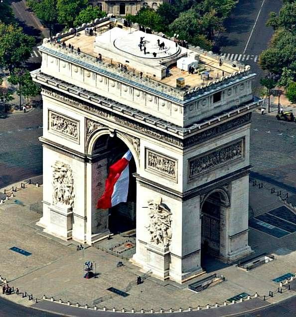 Aerial view of the Arc de Triomphe in Paris with a large French flag draped from the arch