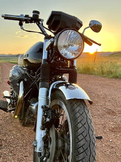 Vintage motorcycle parked on dirt road during sunset with golden sky