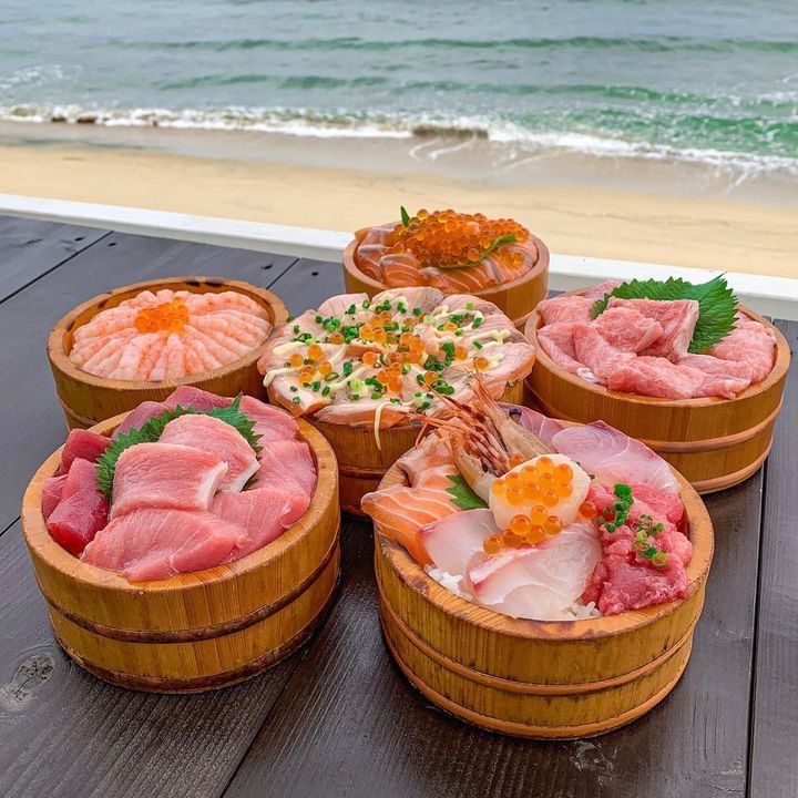 Five wooden sashimi bowls with fresh raw fish and seafood on a table overlooking the ocean