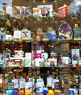 Busy shop window display with mugs, postcards, and Scottish souvenirs on multiple shelves in Inverness